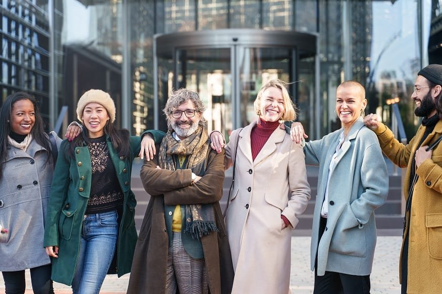 Happy team of elegant business professionals embracing and smiling outside the company workplace. Teamwork, cooperation and success concept